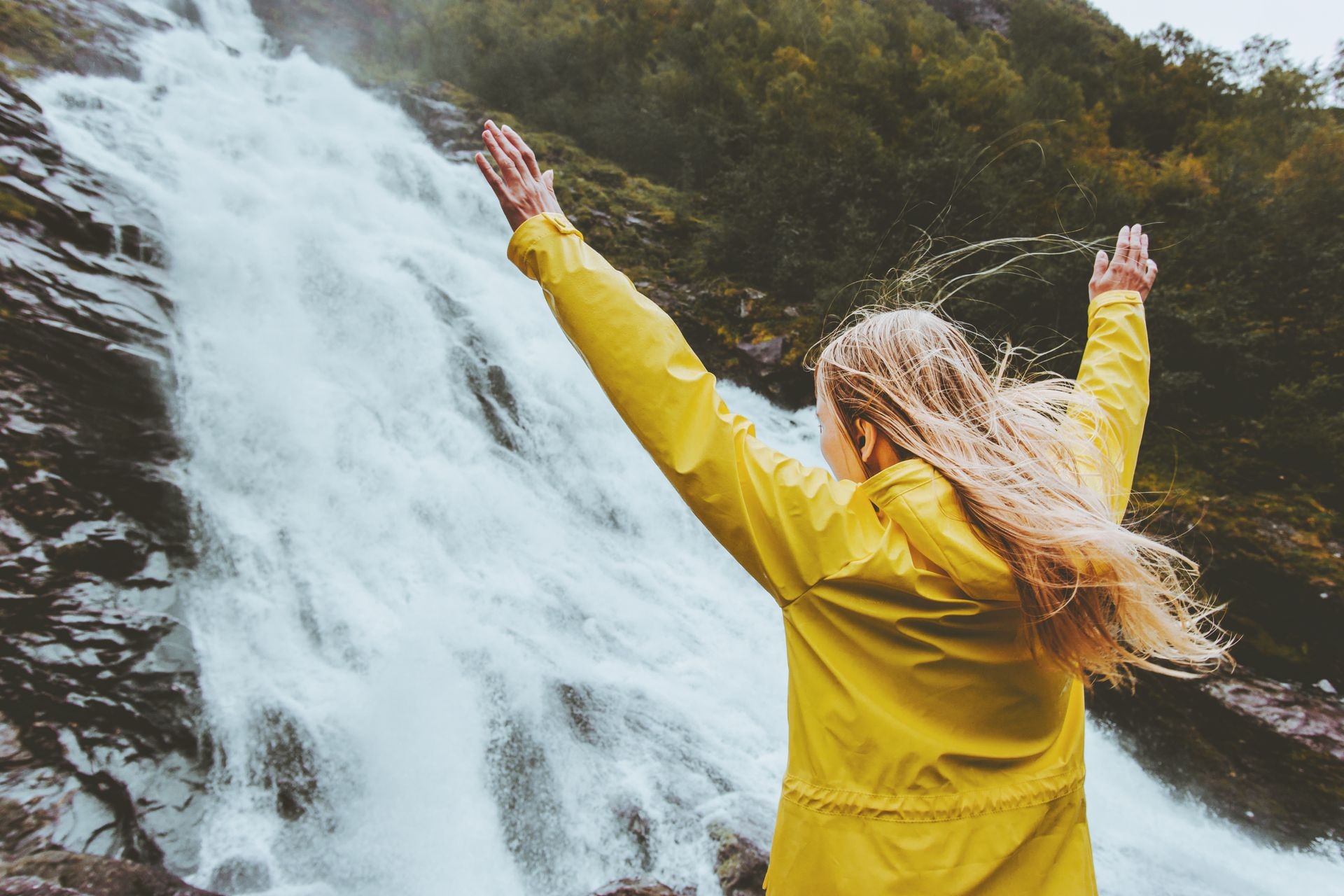 Traveler woman raised hands enjoying waterfall landscape Traveling alone into the wild adventure lifestyle harmony with nature concept emotional expression